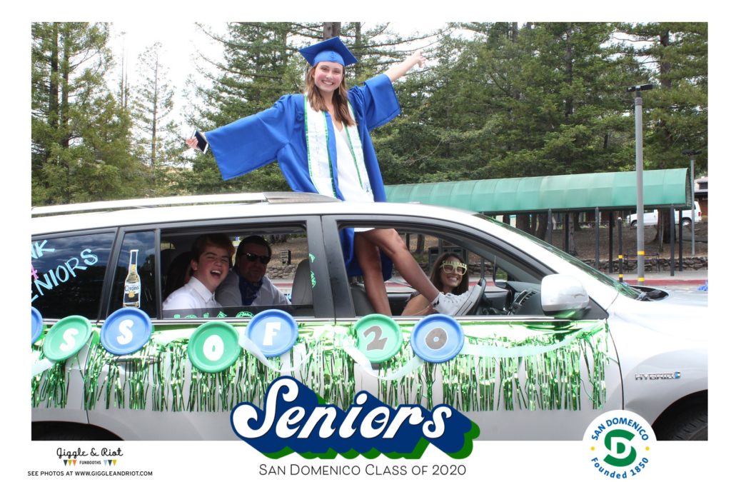 student poses out of sunroof of care for graduation drive thru booth