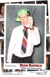 man poses for photobooth with phone prop and green hat