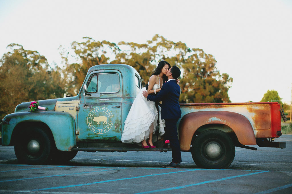 bride and groom kiss in front of vintage truck at hybrid wedding 