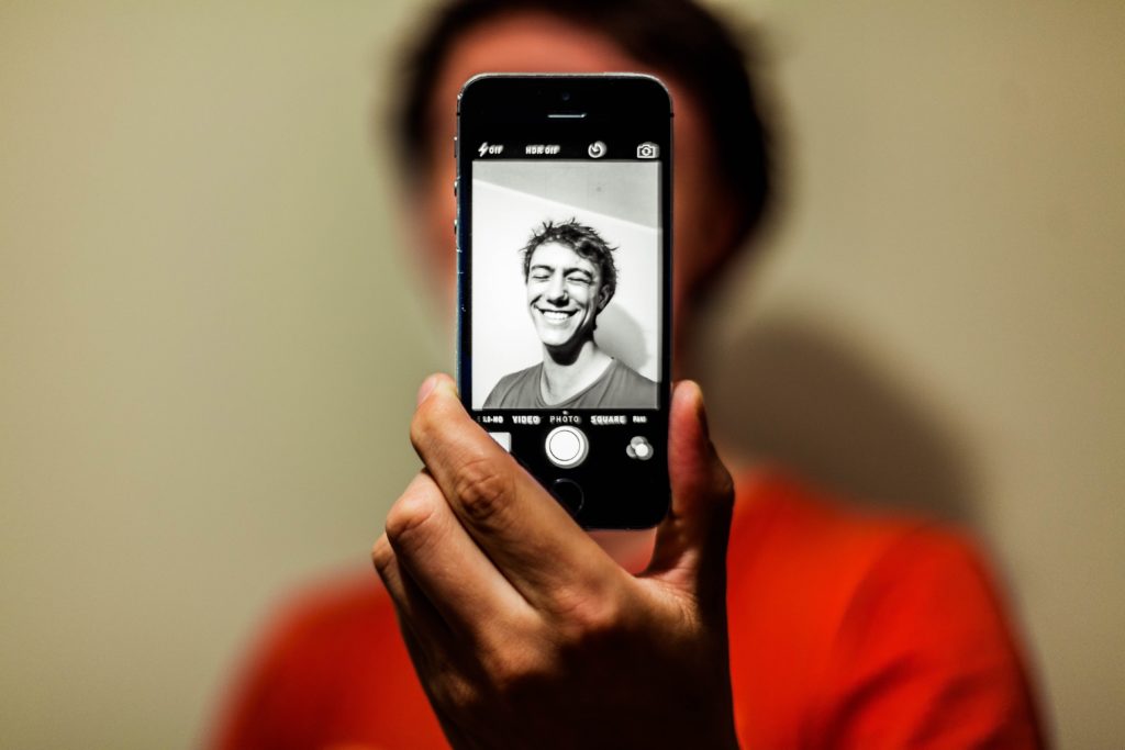man holding up iphone taking selfie 