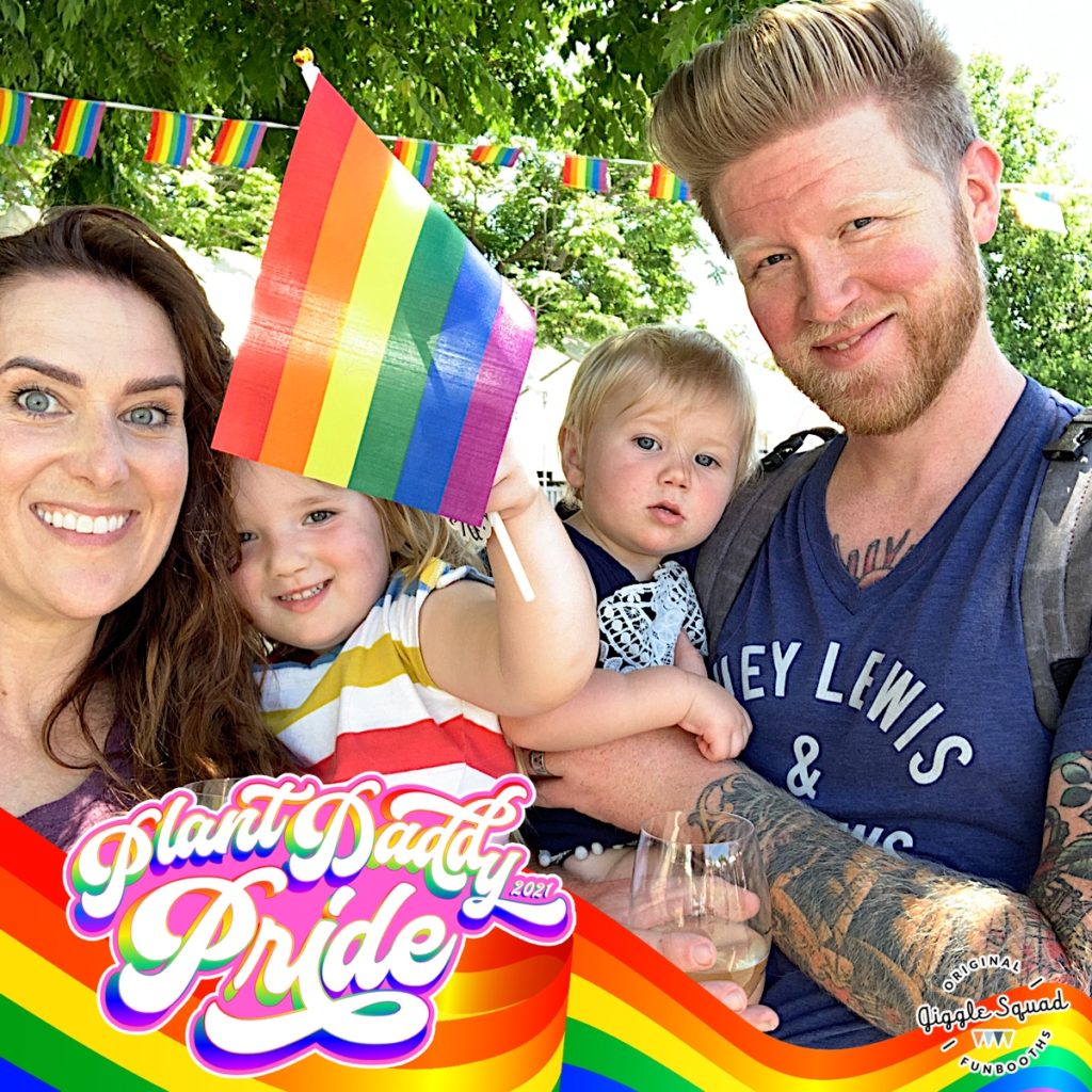 a family with two small children pose for photobooth with rainbow flag and frame