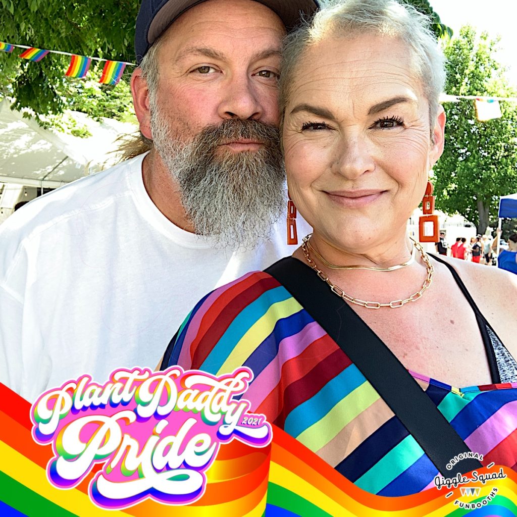 a man and woman pose for photobooth with rainbow frame