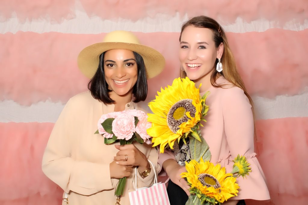 two women with big flowers pose on pink fluffy photobooth backdrop